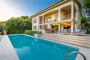 Una casa a due piani con piscina, area salotto esterna e un balcone.