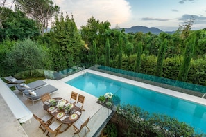 Una piscina con bordo in vetro, immersa nel verde e con un'area pranzo con mobili da esterno.
