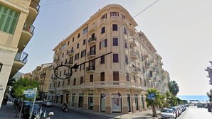 A multi-story building with balconies, a street in front, and parked cars.