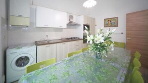 A compact kitchen with a washing machine, a dining table with chairs, and a vase with flowers.