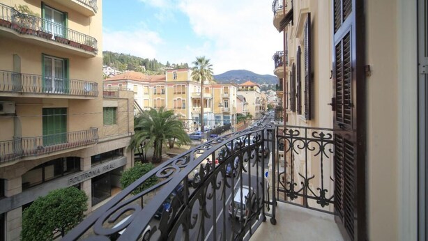 A balcony with wrought iron railings overlooking a street with buildings and a mountain in the background.