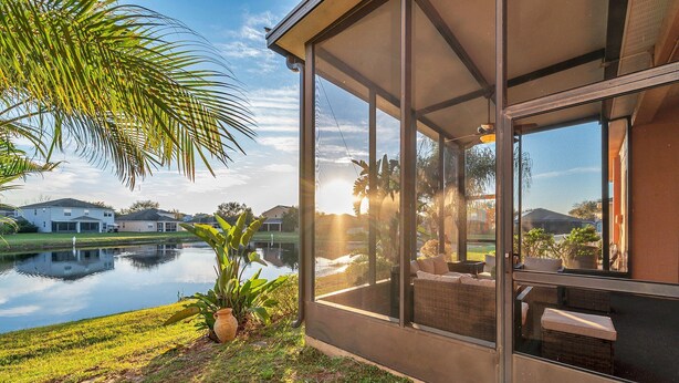 Una casa moderna con amplios ventanales que dan a un lago tranquilo, rodeada de vegetación y un cielo despejado.