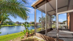 Un porche cerrado con vista a un lago, rodeado de follaje y casas.