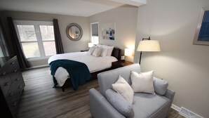 Ein Hotelzimmer mit einem Bett, einem grauen Sofa, einem Schminktisch, einer Lampe und einem Fenster mit Vorhängen.