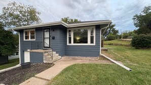 Ein Bungalow mit Veranda, einer kleinen Treppe und einem gepflegten Rasen.