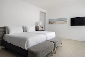 A double bed with a grey bench, a bedside table with a lamp, a painting, and a TV on the wall. - Lagoon Villa 5 Bedroom Including Guesthouse LV17 (Providenciales)