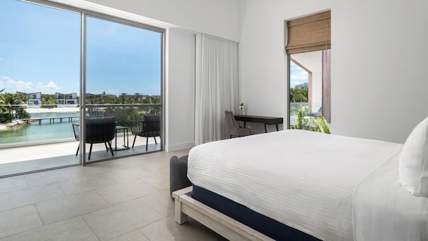 Een moderne hotelkamer met een groot bed, een bureau en uitzicht op een zwembad en gebouwen.
