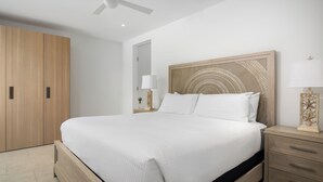Een moderne slaapkamer met een groot bed, een houten garderobe, nachtkastje met lamp en plafondventilator.