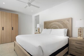 A modern bedroom with a large bed, wooden wardrobe, bedside table with lamp, and ceiling fan.
