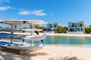 Une plage bordée d’une rangée de canoës, avec un complexe hôtelier moderne en arrière-plan.