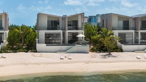 Un hotel moderno frente a la playa con edificios de varios pisos, asientos al aire libre y una vista despejada del océano.
