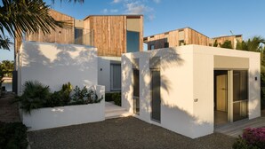 Een modern huis met een minimalistisch ontwerp, met een combinatie van houten en witte wanden, grote ramen en een kleine tuin met planten en een grindpad.