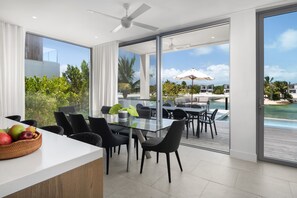 A modern dining area with a glass table, black chairs, and a view of the ocean and resort buildings.