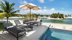 Een zwembadterras met ligbedden, een sofa en een parasol, met uitzicht op een strand en de oceaan.