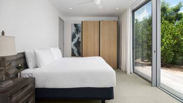 A modern bedroom with a large bed, a wooden headboard, a nightstand, and a large window with a view of greenery.