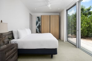 Una camera da letto moderna con un letto grande, una testiera in legno, un comodino e un'ampia finestra con vista su del verde.