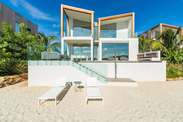 Uma casa moderna à beira-mar com escada de vidro, área de estar externa e vista para o oceano.