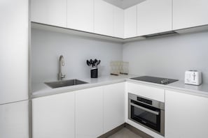 Una cucina moderna con mobili bianchi, un lavello in acciaio inossidabile, forno integrato e un tostapane.