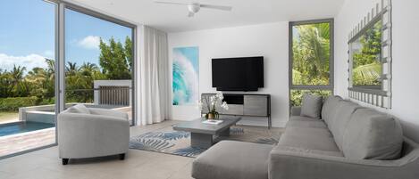 A modern living room with a large window, a flat-screen TV, and a pool view.