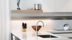 Une cuisine moderne avec un îlot central, des tabourets de bar blancs, un luminaire suspendu et une plante en pot.