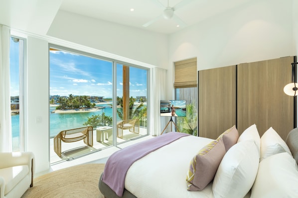 Un dormitorio moderno con una cama grande, vistas a una playa y al océano, y un balcón con una silla y una mesa.