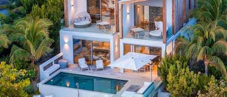 A modern two-story house with a swimming pool, outdoor seating, and lush greenery.