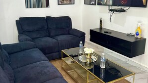 Un salon comprenant un canapé d’angle, une table basse en verre, un téléviseur à écran plat et des œuvres d’art encadrées accrochées au mur.