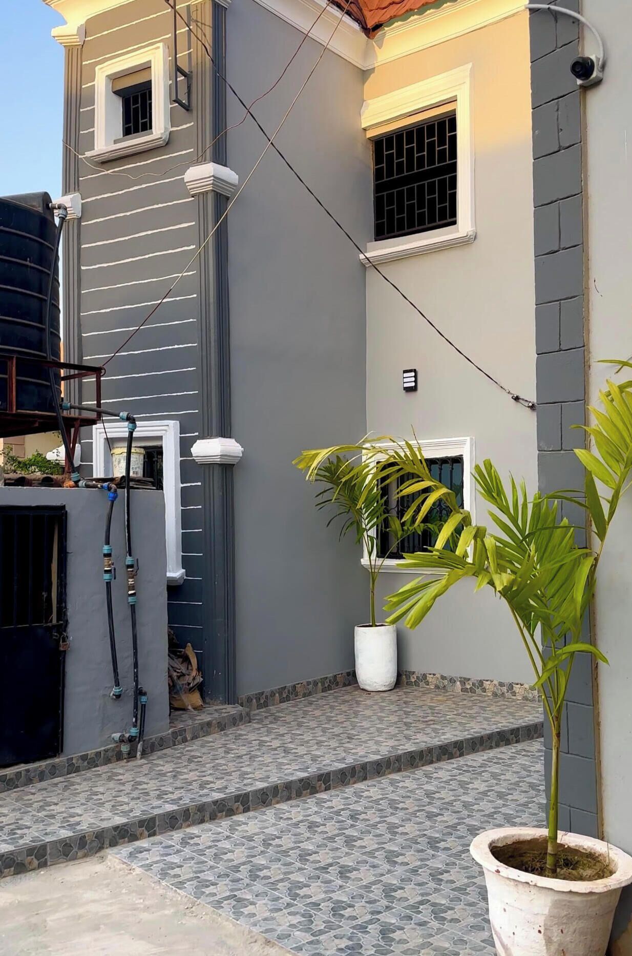 Zona residencial con patio empedrado, un tanque de agua y plantas en macetas.
