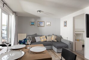Uma sala de estar moderna com um sofá seccional cinza, uma mesa de jantar posta com pratos e talheres, e quadros nas paredes.