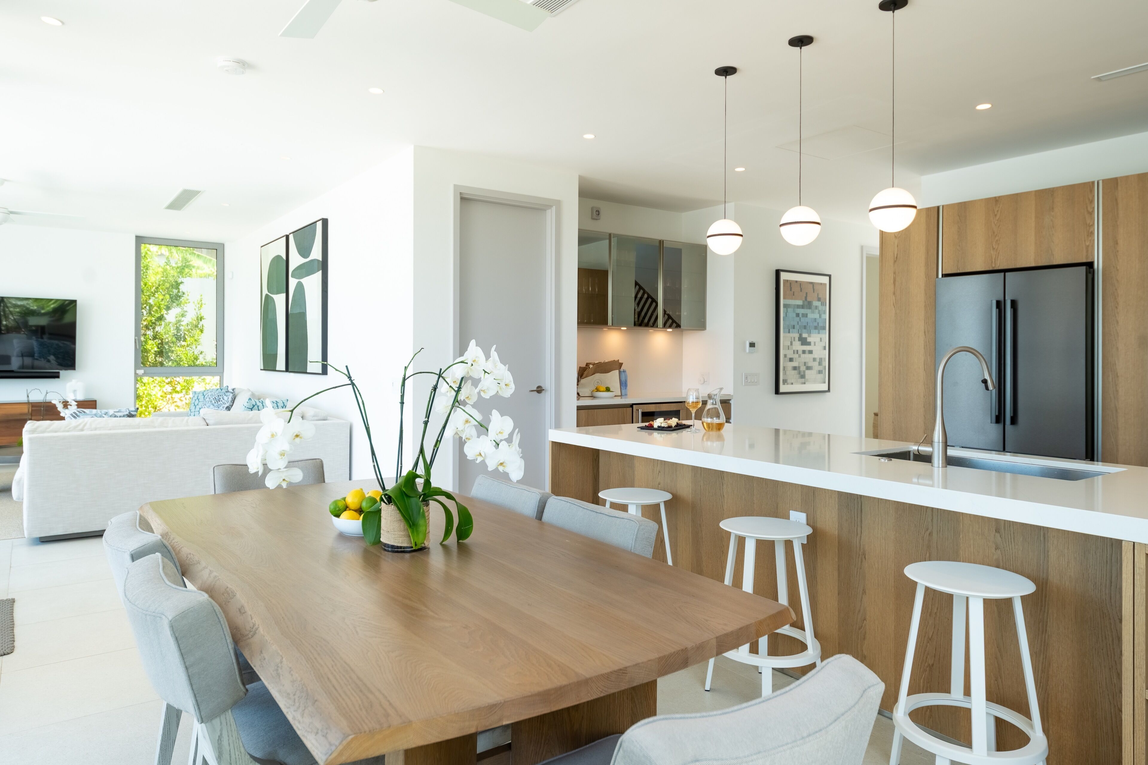 Uma cozinha moderna com ilha central, banquetas e uma mesa de jantar com cadeiras.