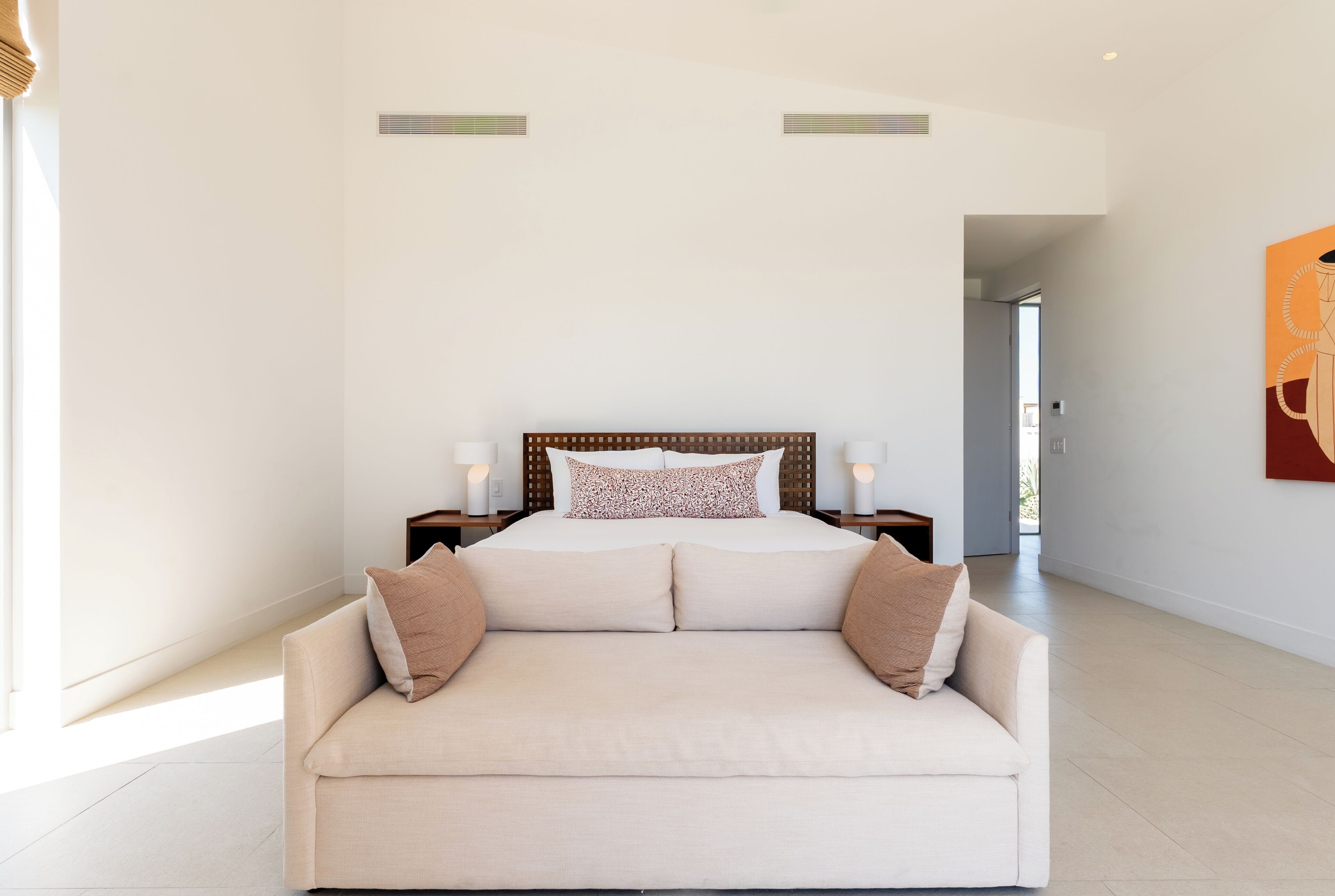 Een slaapkamer met een bed, een bank, twee nachtkastjes en een deur naar een andere kamer.