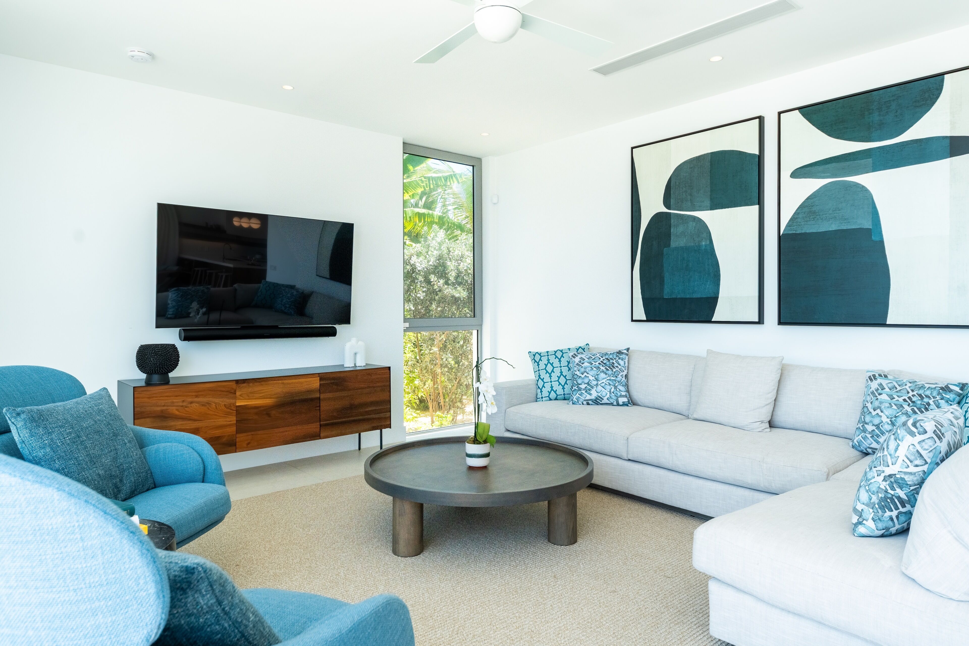 A modern living room with a grey sofa, blue armchairs, a coffee table, and abstract wall art.