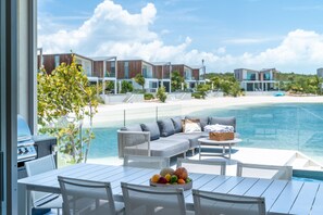 A poolside area with a dining table, chairs, a sofa, and a fruit bowl. - Lagoon Villa 3 Bedroom LV14 (Providenciales)