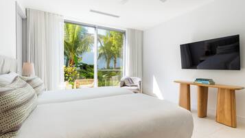 A hotel room with a large bed, a TV mounted on the wall, and a balcony with a view of palm trees.