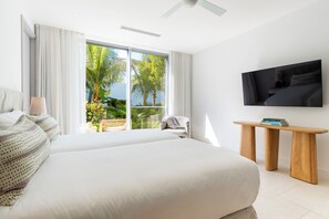 Une chambre d’hôtel avec un grand lit, un téléviseur fixé au mur et un balcon offrant une vue sur les palmiers.