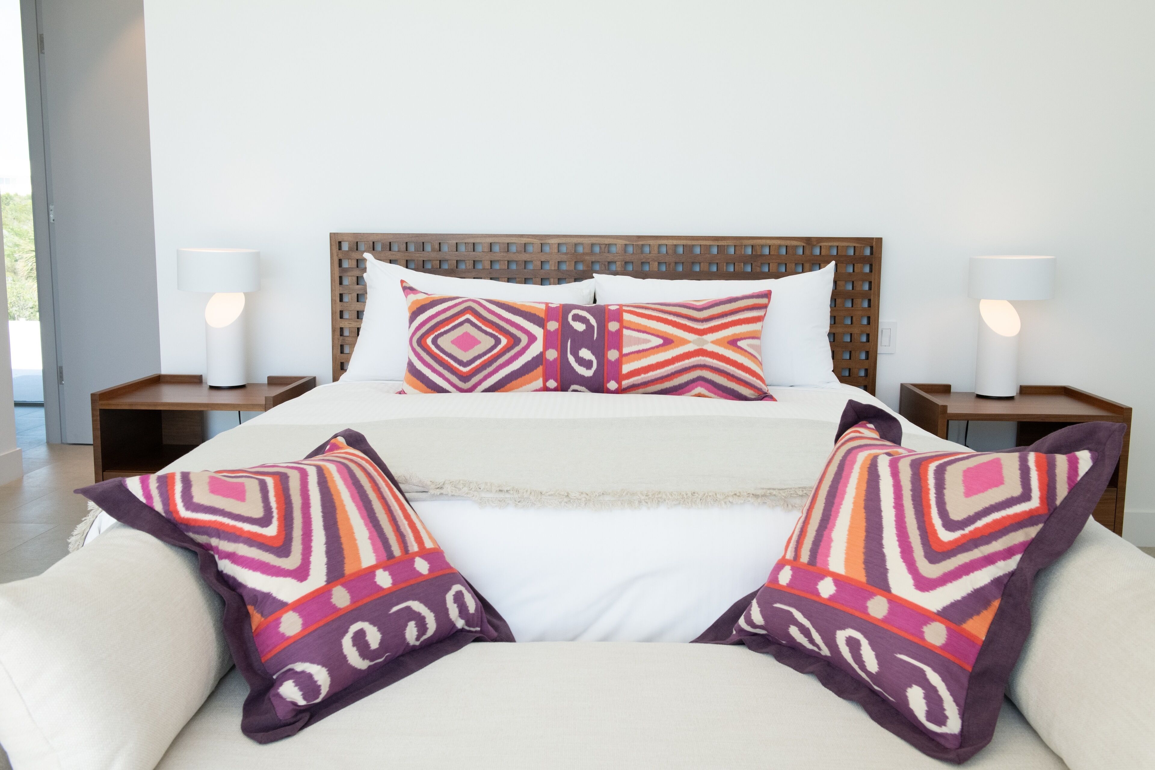 Una cama con cabecera de madera, dos mesitas de noche con lámparas y varias almohadas estampadas.