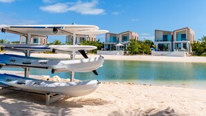 A beach with a row of sea kayaks and a modern resort building with multiple balconies.