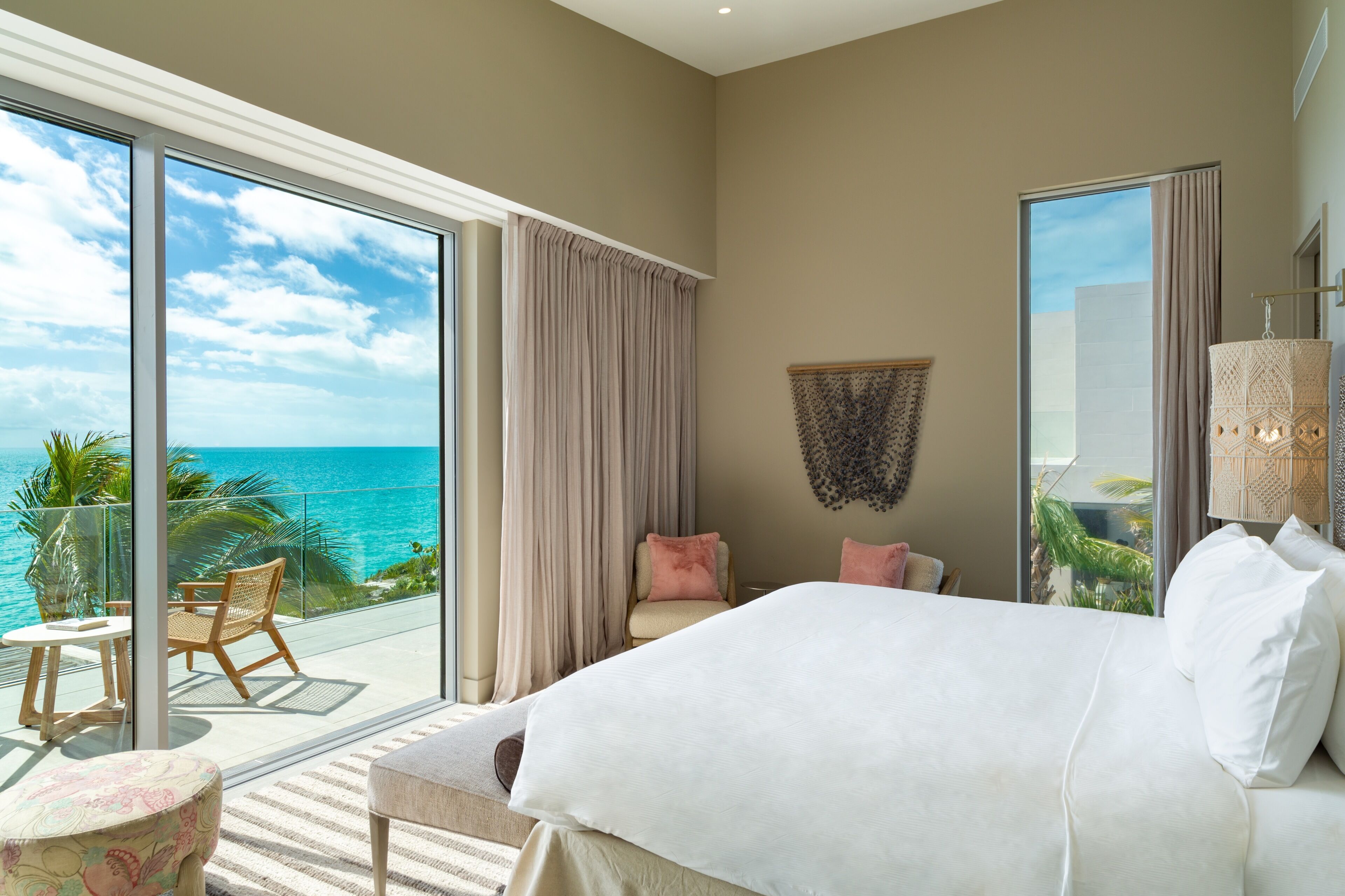 A bedroom with a large bed, a balcony with a view of the ocean, and a seating area with a table and chairs.