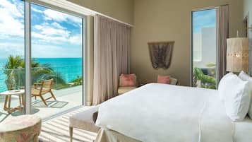 A bedroom with a large bed, a balcony with a view of the ocean, and a seating area with a table and chairs.
