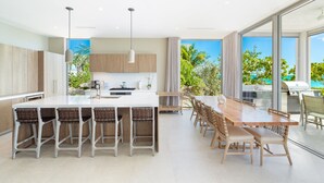 A modern kitchen with a central island, bar stools, and a dining area with a large table and chairs. - Ocean Estate Reef 5 Bedroom Including Guesthouse OE10 (Providenciales)