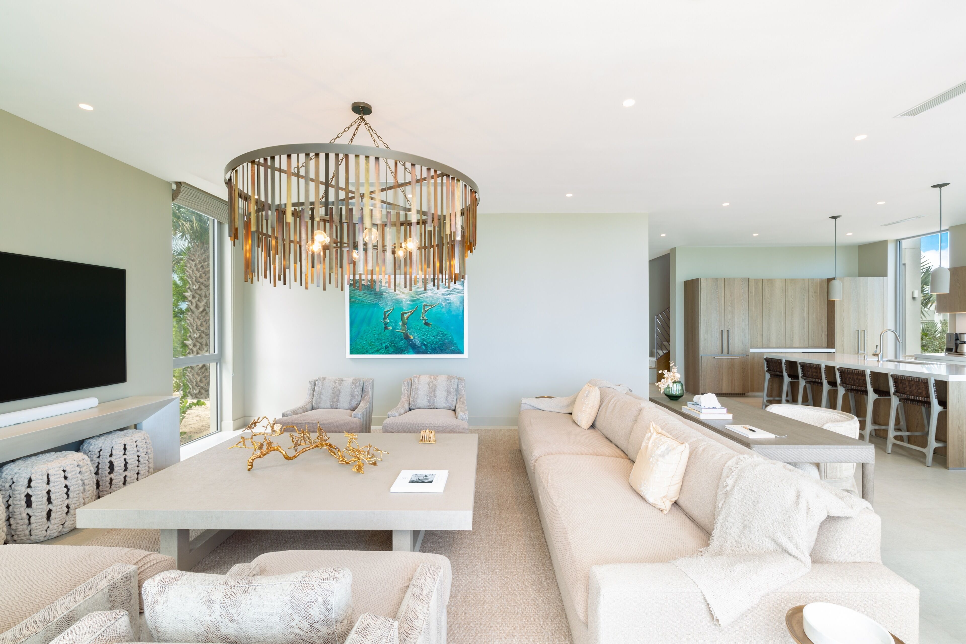 A modern living room with a large flat-screen TV, a dining area with a central table, and a kitchen with a bar.