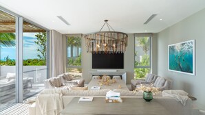 A modern living room with a large TV, comfortable seating, and a view of the outdoors. - Ocean Estate Reef 5 Bedroom Including Guesthouse OE10 (Providenciales)