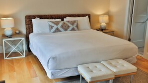 A neatly arranged bedroom with a large bed, two bedside tables with lamps, and a small bench.