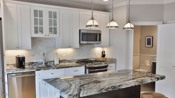A modern kitchen with white cabinets, a stainless steel dishwasher, a built-in microwave, and a marble countertop.
