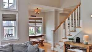 A spacious living area with a grey sofa, wooden bench, and a staircase with white railings.