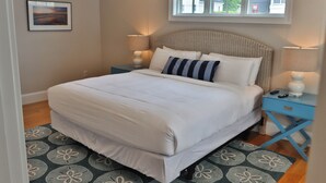 A neatly made bed with white bedding, two bedside lamps, a blue nightstand, and a patterned rug.