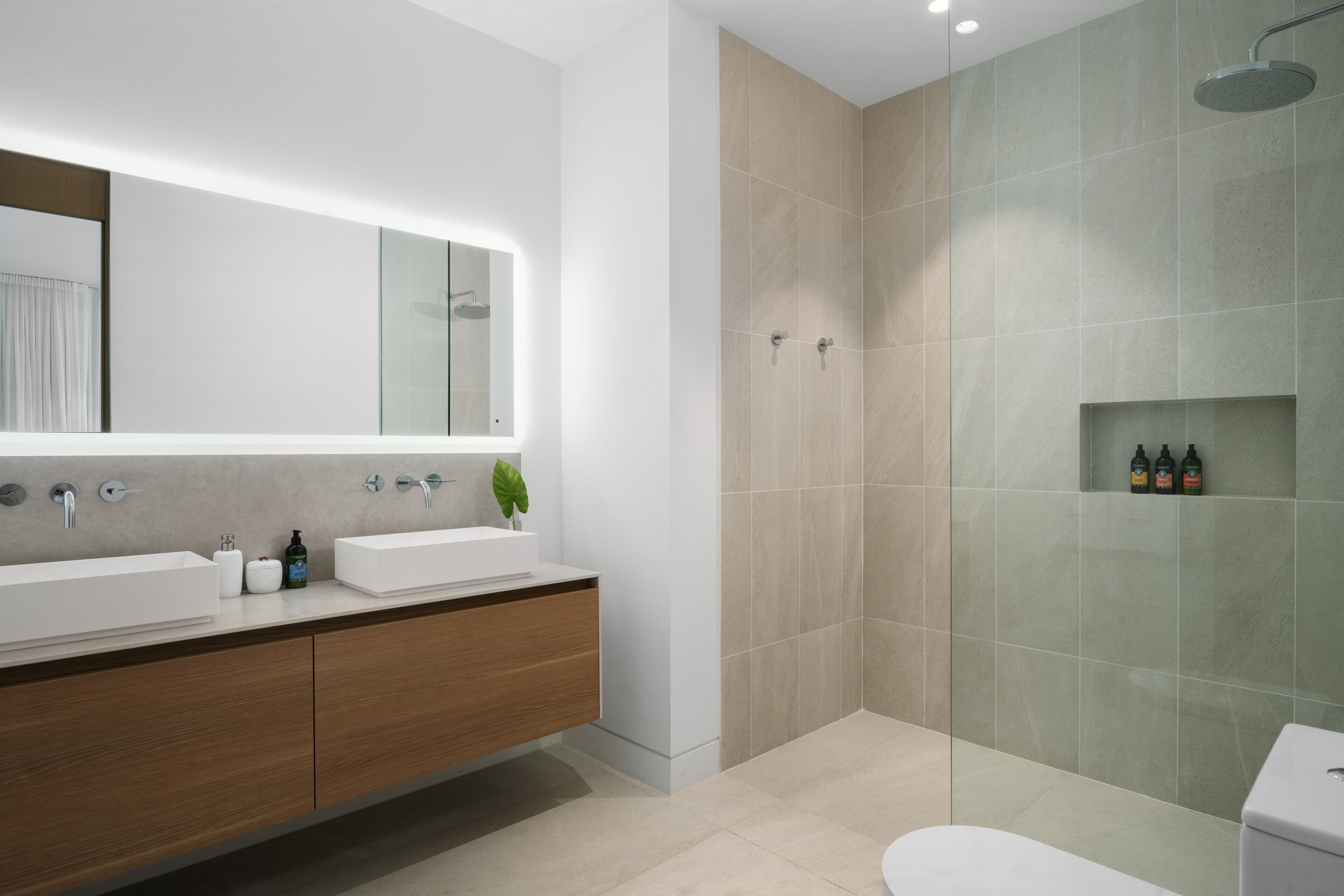 A modern bathroom with a double sink vanity, a large mirror, a shower area, and a toilet.