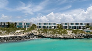 Ein modernes Resort mit mehreren zweigeschossigen Gebäuden, einer felsigen Küstenlinie und klarem türkisblauem Wasser.