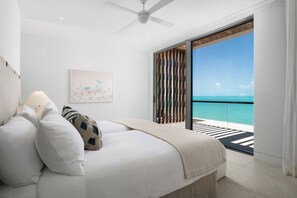 A bedroom with a bed, a ceiling fan, a window with a view of the ocean, and a painting on the wall.