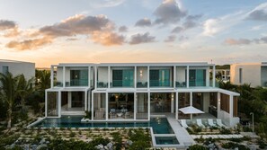 A modern multi-story house with a swimming pool, outdoor seating, and a view of the sea.